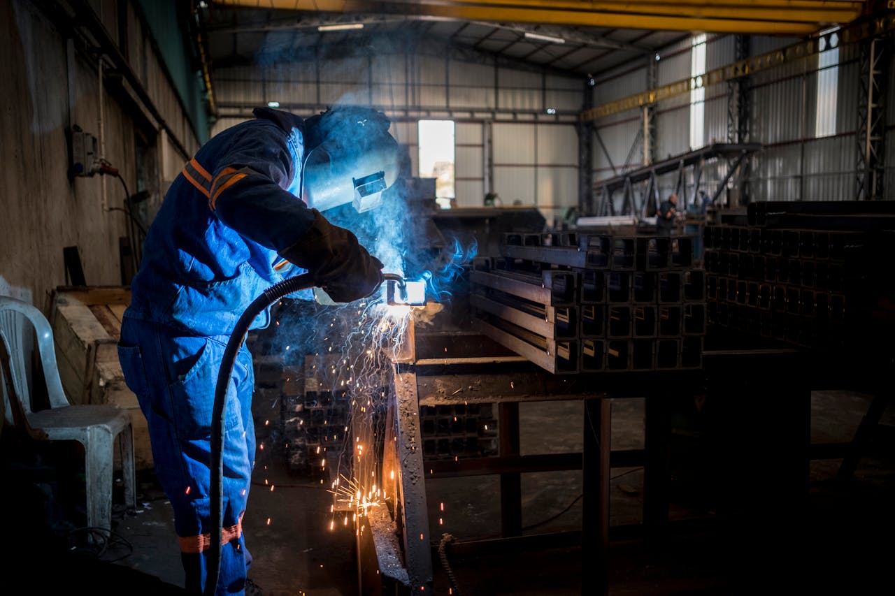 Worker in a PPE welding steel collumns in a factory.