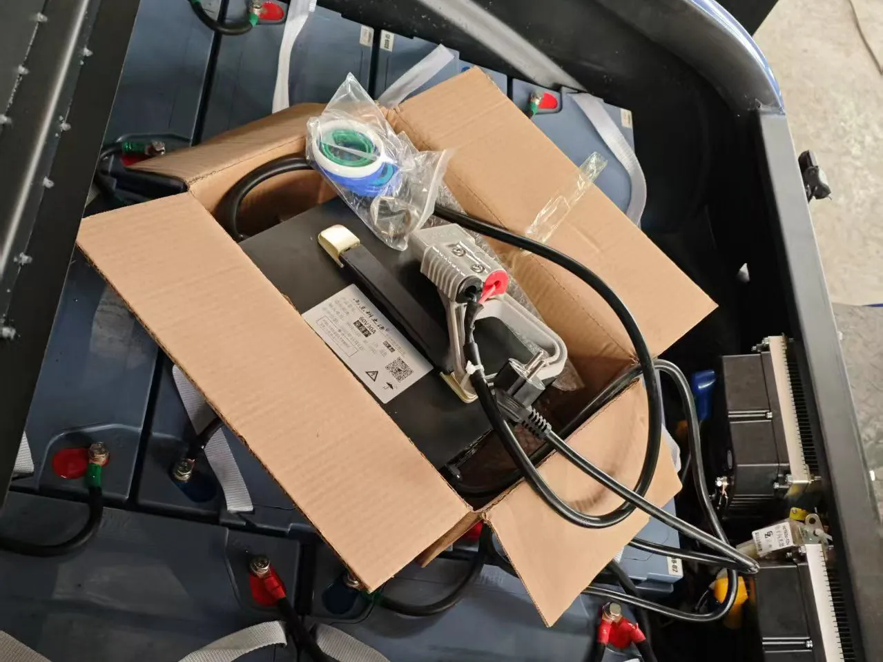 Electric forklift engine bay with battery and battery connections visible, hood open